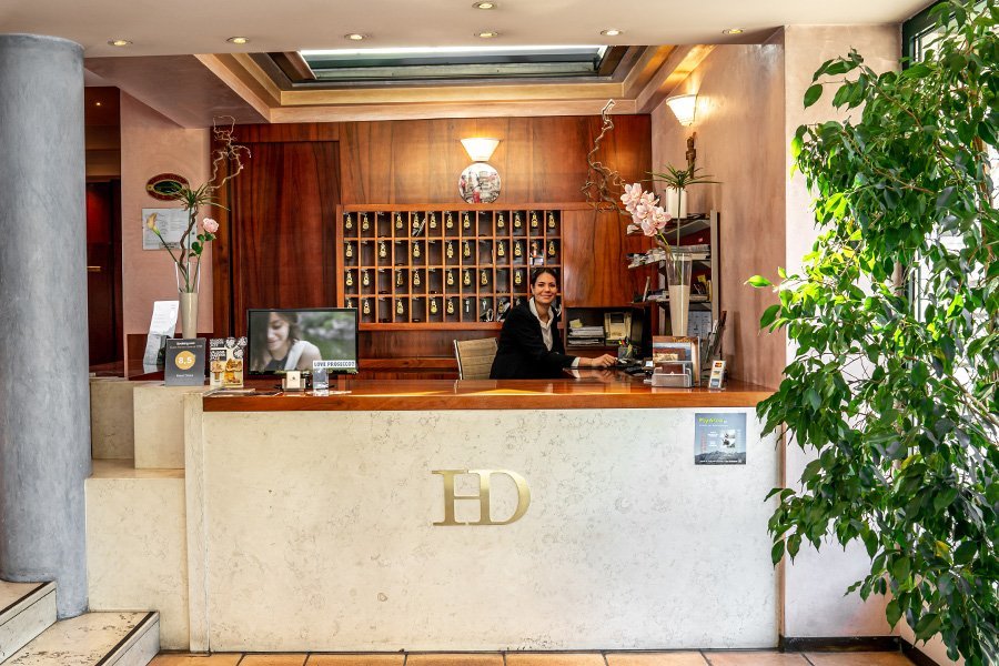 La reception dell'Hotel Diana con il logo HD e una receptionist sorridente