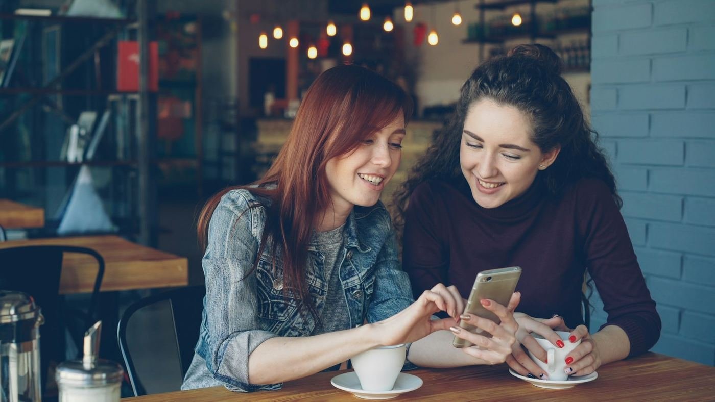 Due amiche al bar guardano insieme uno smartphone